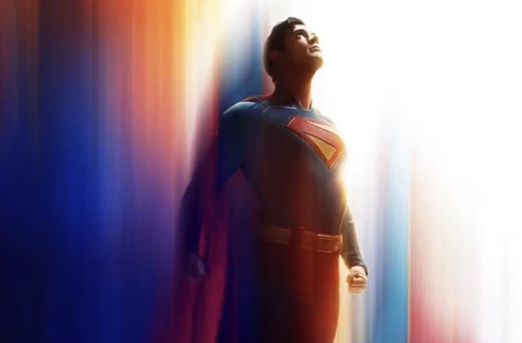 Superman stands heroically, looking upward toward a bright light, with a blurred, colorful background blending blue, orange, and white tones